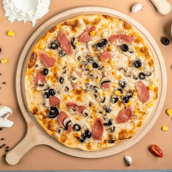 A Paras Pizza & Gyro pizza with sausage, mushrooms, olives, and corn on a wooden peel.