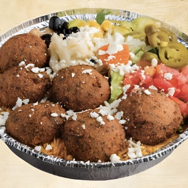 A foil container filled with falafel, rice, feta cheese, black olives, tomatoes, and pickled jalapeños.